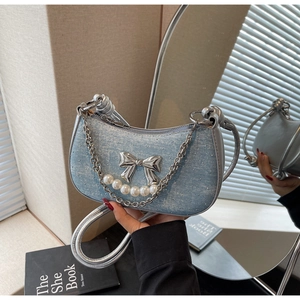 Detail of light blue denim crescent bag with silver bow and pearl chain accessories