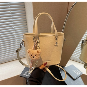Detail of cream white litchi grain bucket bag with cute plush bear charm and strap