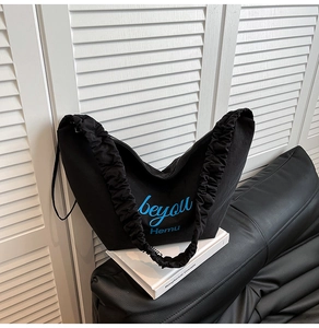 Detail of black crescent canvas tote bag with pleated shoulder strap and blue text