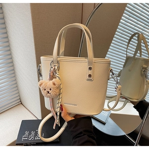 Detailed close-up of cream-colored litchi grain leather tote bag with teddy bear charm