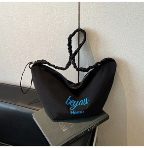 Detail of black canvas shoulder bag with blue embroidery and pleated strap on a book