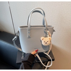 Detail of light gray lychee grain bucket bag with cute plush bear charm and brand logo