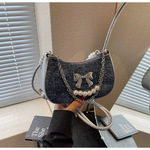 Detail of blue denim underarm bag with silver bow and pearl chain decoration