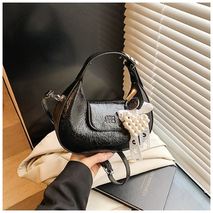 Detail of black pleated leather handbag featuring pearl heart charm and metal lettering