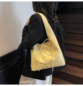 Détail d'un grand sac cabas jaune en cuir avec nœud décoratif porté par un mannequin