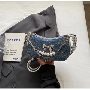 Close-up of blue denim crescent bag with silver bow, pearls, and knotted metal hardware