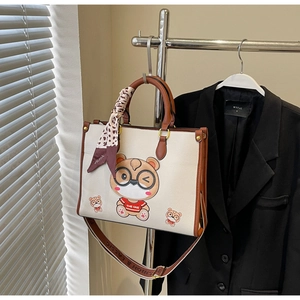 Close-up of beige bear tote bag with leopard scarf and litchi grain leather texture