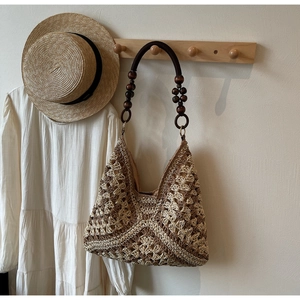Detail of woven straw tote bag featuring dark wooden bead handles and a hollow pattern