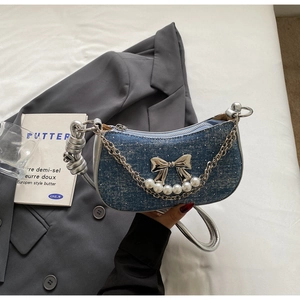 Detail of denim shoulder bag featuring a silver metal bow and white pearl accents