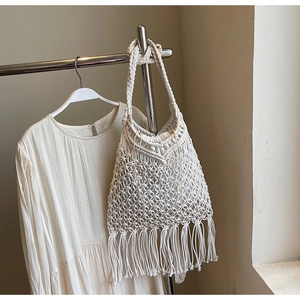 Close-up of white bohemian woven tote bag with long tassel details and hollow pattern