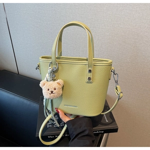 Detail of light green bucket bag with lychee texture and cute teddy bear charm
