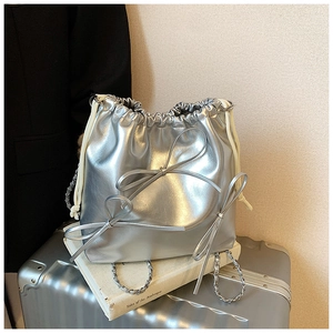 Detail of silver bucket bag with ribbon bows and metallic chain on a suitcase
