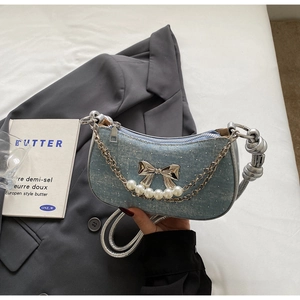 Detail of denim blue underarm bag featuring silver bow, pearl chain and rhinestone studs