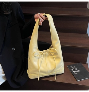 Détail d'un sac à bandoulière jaune pâle avec un long nœud à cordon sur un escalier noir