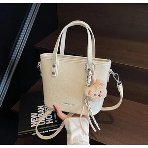 Detailed macro view of cream pebbled leather bucket bag with a cute brown teddy bear charm