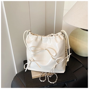 Detail of cream white bucket bag featuring elegant ribbon bows and chain strap texture