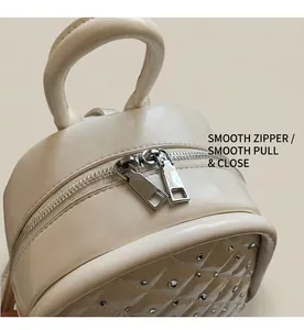 Macro detail of smooth silver double zippers and quilted texture on off-white mini backpack