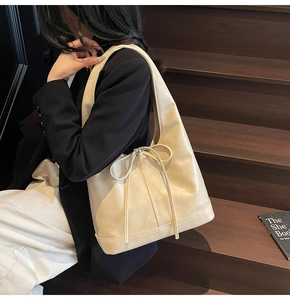 Détail du sac cabas en cuir crème avec cordon à nœud porté à l'épaule par un mannequin