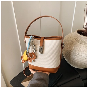 Detail of woven bucket bag with brown leather trim, metal lock and elephant charm