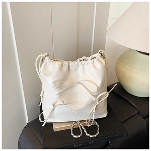 Detail of cream drawstring bucket bag with decorative bows and metallic chain strap