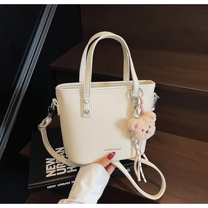 Close-up of white pebble leather handbag with silver logo and pink plush bear charm