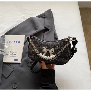 Close-up of black tweed underarm bag with silver bow charm and elegant white pearls