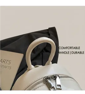 Close-up of cream quilted backpack featuring top handle and dual metal zipper detail