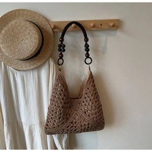 Close-up of bohemian woven straw bag with unique dark wooden beaded handle detail