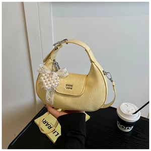 Detail of yellow pleated leather handbag with pearl heart charm and lace bow decoration