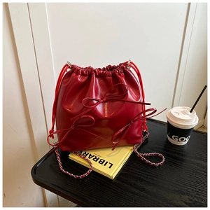 Red glossy bucket bag with double bow accents and chain strap on a black desk