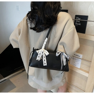 Detail of black lychee leather crossbody bag with white lace bow and checkered ribbon