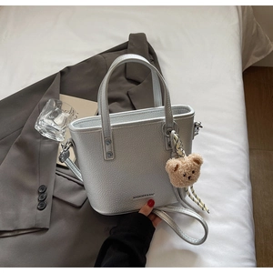 Silver bucket bag with plush bear charm on dark suit and white bedding