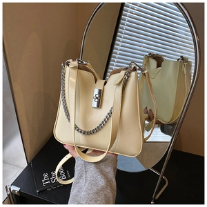Detail view of cream bucket bag with metal twist lock and chain strap against a mirror