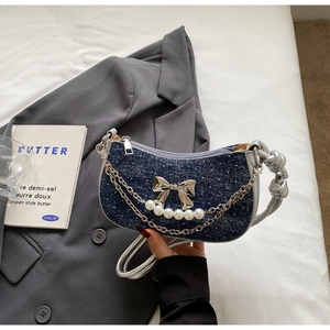 Detail of blue denim hobo bag with silver bow charm, pearls and knotted strap details