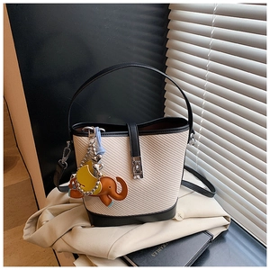 Detail of woven bucket bag with black leather trim, metal clasp, and elephant charm
