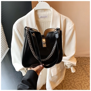 Close-up of black glossy leather bucket bag with metal chain strap and magnetic closure