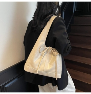 Grand sac cabas crème avec détail de nœud porté à l'épaule sur un blazer noir élégant