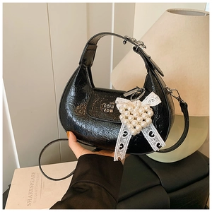 Detail of black semi-circle handbag with heart pearl lace charm and golden zipper