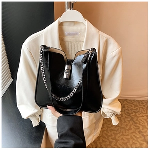 Close-up of black glossy leather bucket bag featuring a silver metal chain and twist lock