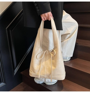 Détail du grand sac cabas beige avec nœud en cuir sur des escaliers en bois
