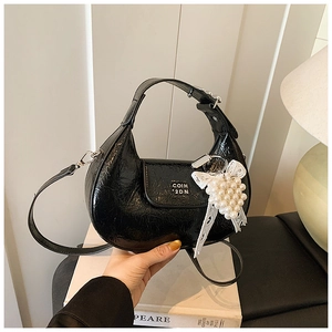 Detail of black patent leather hobo bag with pearl lace charm and silver brand logo