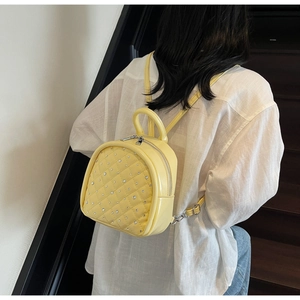 Detail of yellow quilted mini backpack with rhinestone studs on modern woman outfit