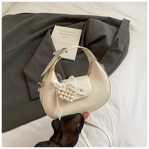 Detail of cream white crescent bag featuring pleated texture and pearl heart pendant