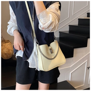 Detail of cream bucket bag with silver chain strap and metal lock shown on a model