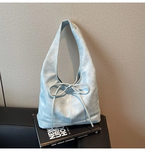 Détail du sac hobo bleu clair avec texture vintage et nœud ruban sur un livre