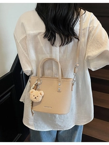 Minimalist beige pebble leather bucket bag with plush bear charm and patterned scarf