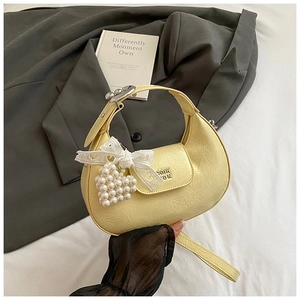 Detail of light yellow crescent bag with pleated texture and pearl heart pendant charm