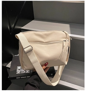 Detail view of beige canvas crossbody bag with multiple zippers and adjustable strap