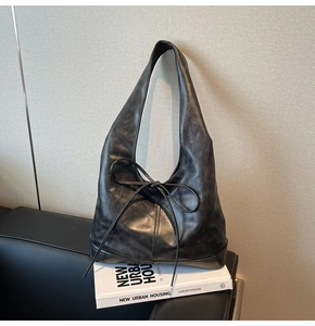 Détail du sac hobo en similicuir noir avec nœud décoratif sur un canapé moderne