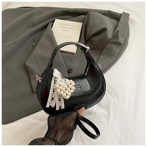 Detail of black patent leather crescent bag with pearl heart charm and lace ribbon
